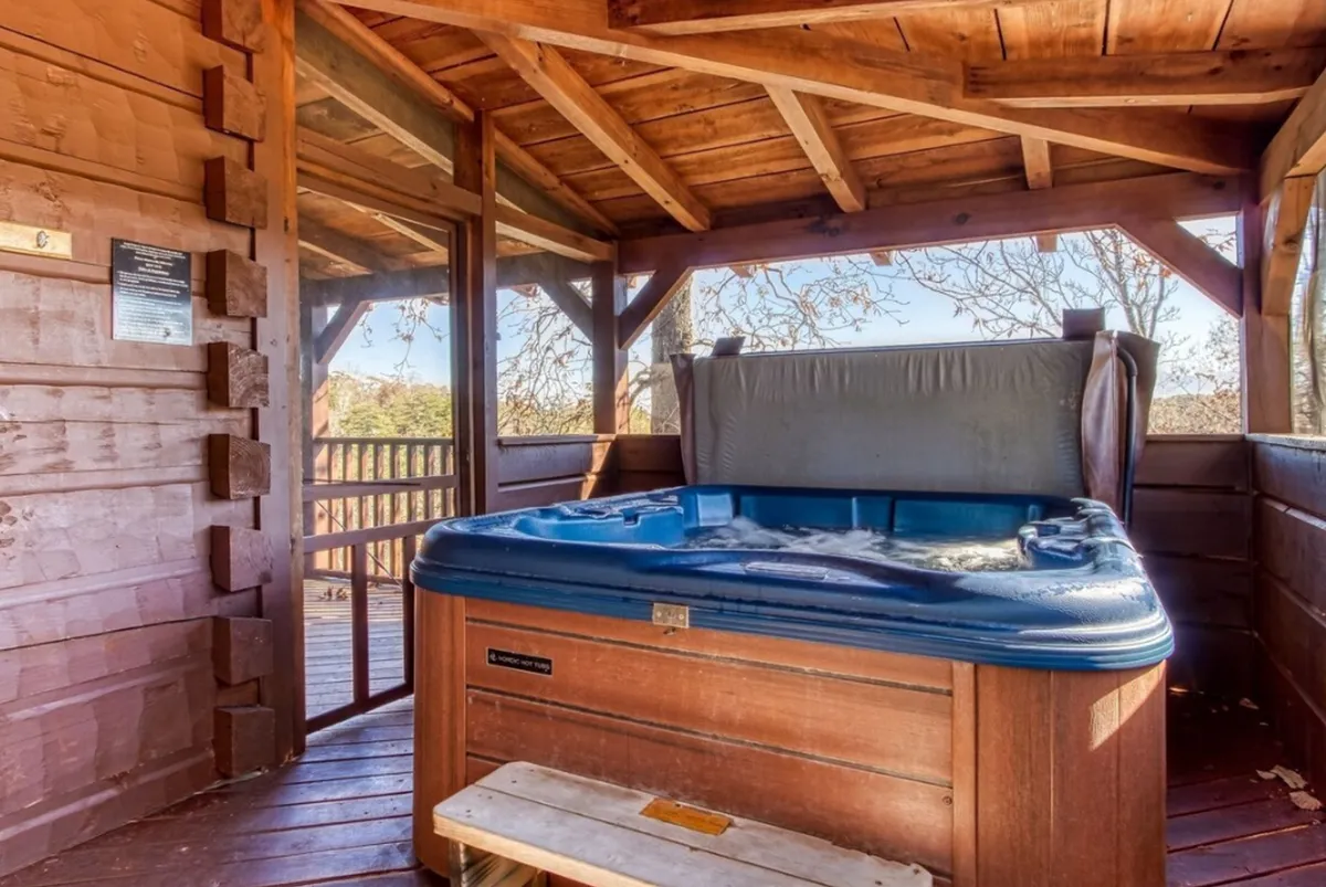 A tranquil interior scene featuring a bubbling hot tub nestled within a wooden structure, surrounded by large windows that frame sweeping mountain views. The space is designed for relaxation and socializing, inviting guests to unwind while soaking in the scenery at sunset or enjoying a peaceful morning.