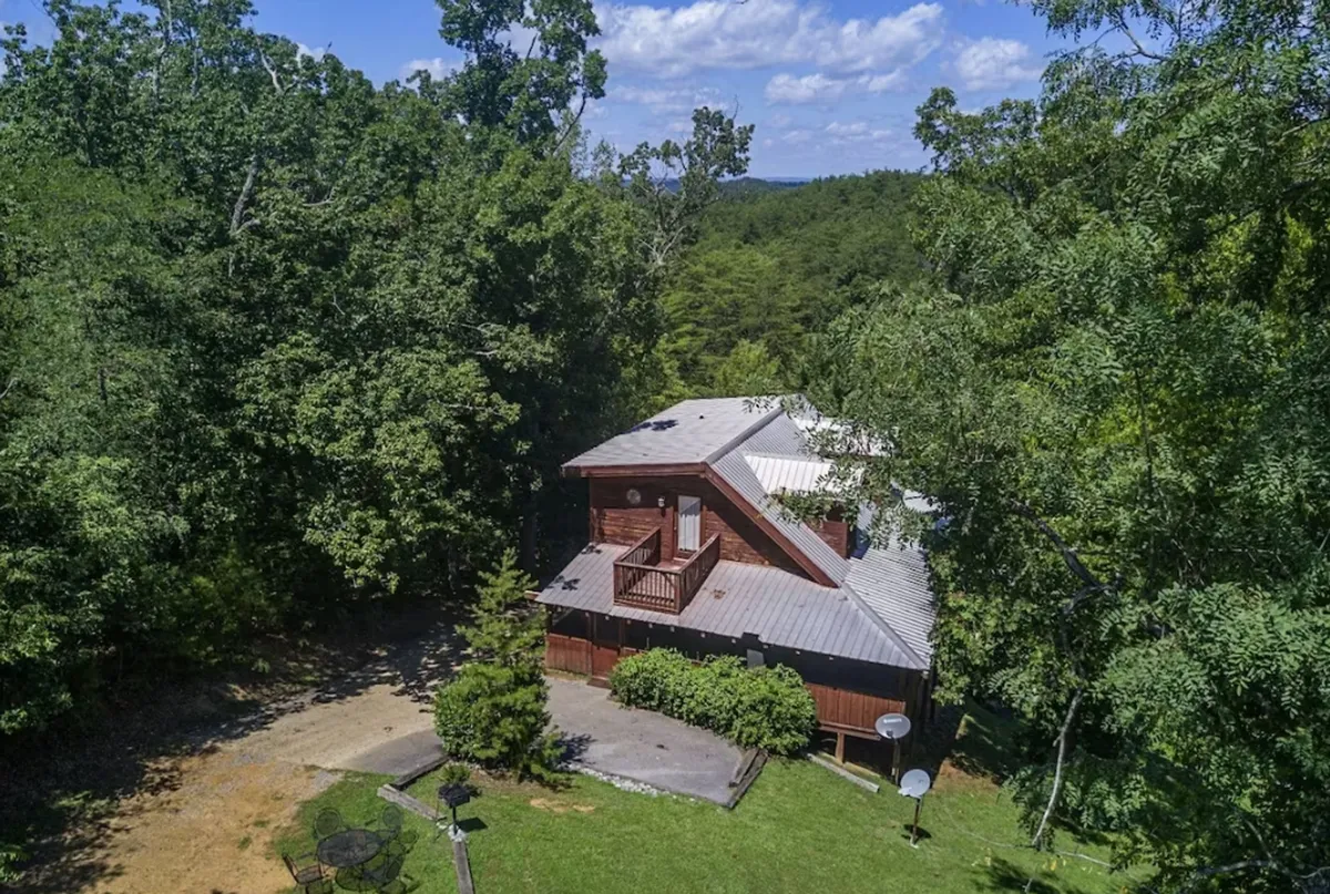 This image depicts the wooden exterior of the house surrounded by trees, with a welcoming balcony area. The setting radiates privacy and seclusion, ideal for romantic getaways and moments of togetherness. The balcony is positioned for viewing sunsets or stargazing, connecting the home to its tranquil mountain surroundings.