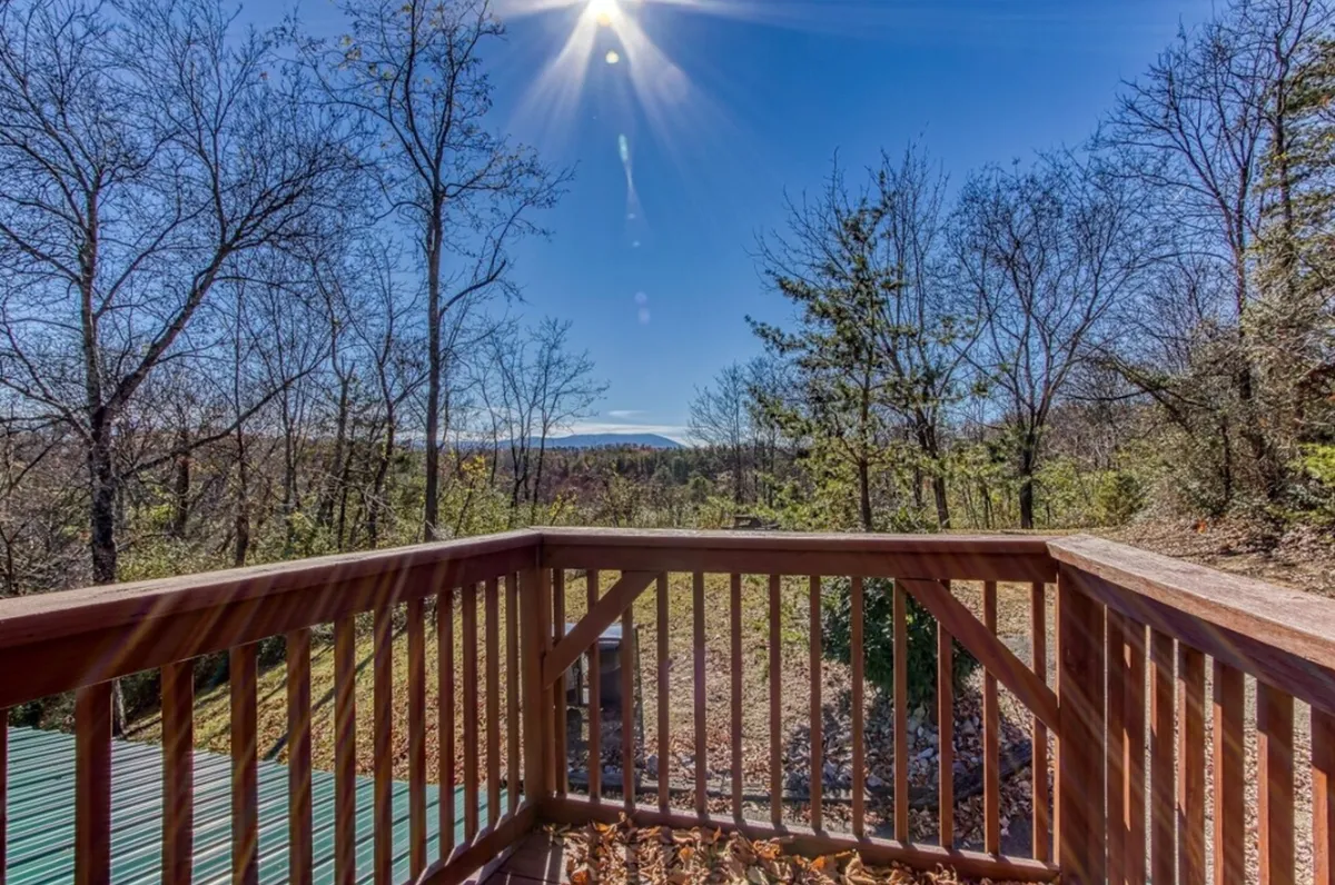 A peaceful deck with a railing frames distant mountains under a clear sky with bare trees, suggesting a serene spot for morning coffee, birdwatching, or stargazing. The view epitomizes the mountain magic and tranquility promised for couples seeking both privacy and adventure.