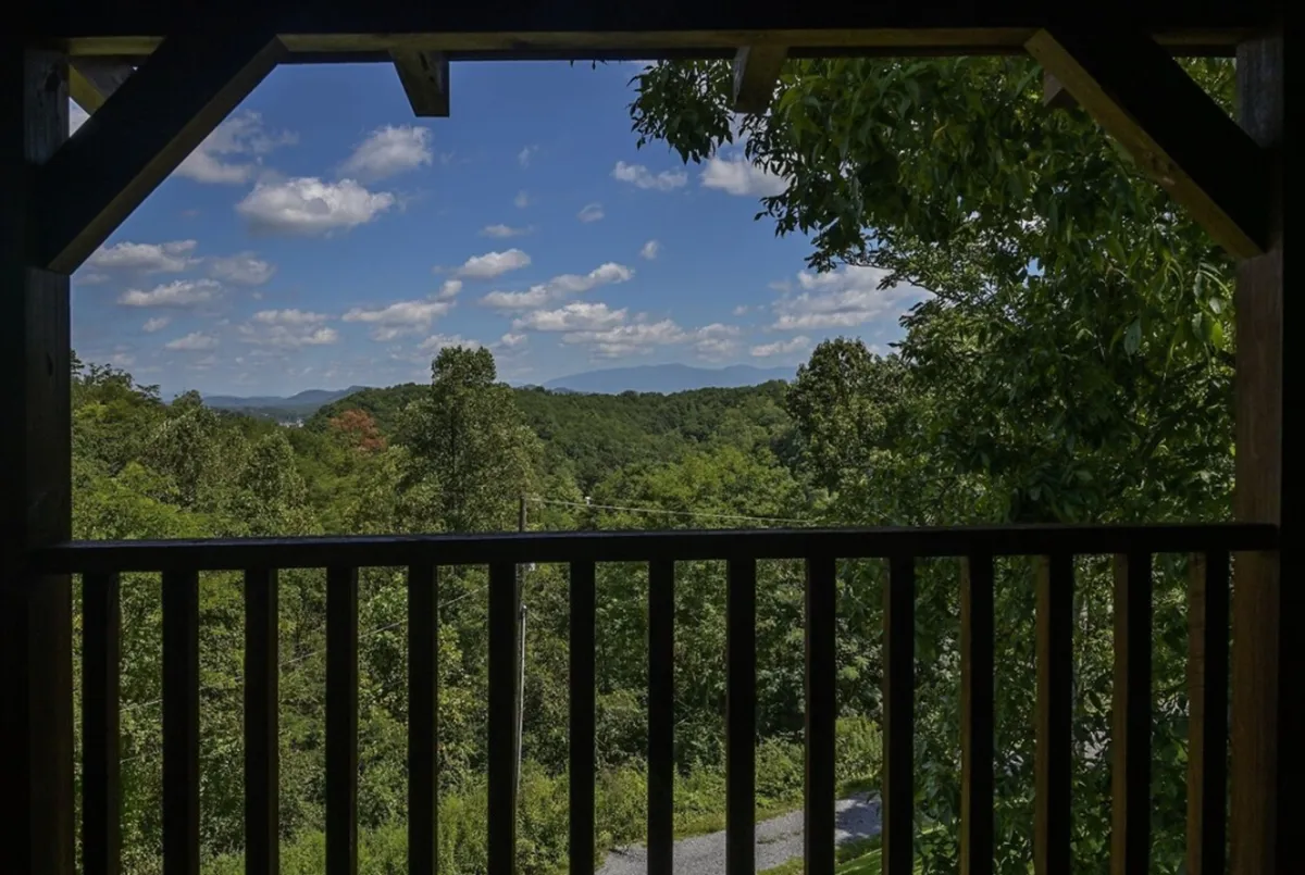 A stunning view of the Smoky Mountains, lush greenery, and a cloudy sky, seen from an outdoor vantage point like a balcony or deck. The image captures the serene, expansive landscape that guests can enjoy during their stay.