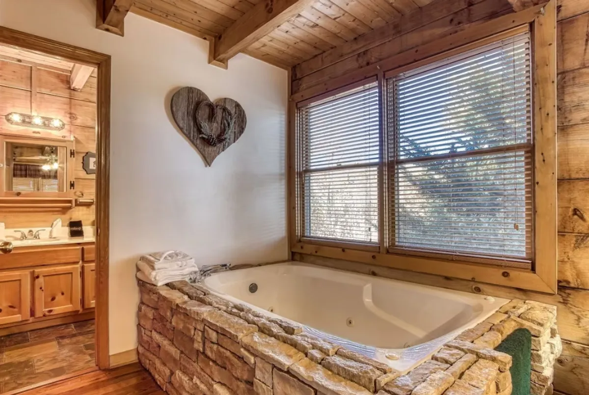 The image presents a tranquil bathroom featuring a spacious jacuzzi tub accented by wooden walls and heart-shaped decor. Natural light and thoughtful details evoke a personal spa experience.
