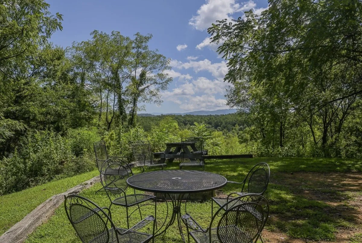 A metal table and chairs are set on a patio overlooking distant hills, offering a peaceful spot for outdoor dining, socializing, and enjoying nature. The scene evokes moments of shared meals, sunset views, and stargazing with friends.